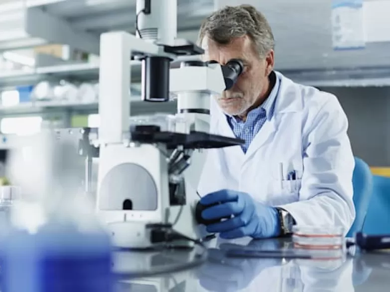 lab technician using microscope dressed in white lab coat