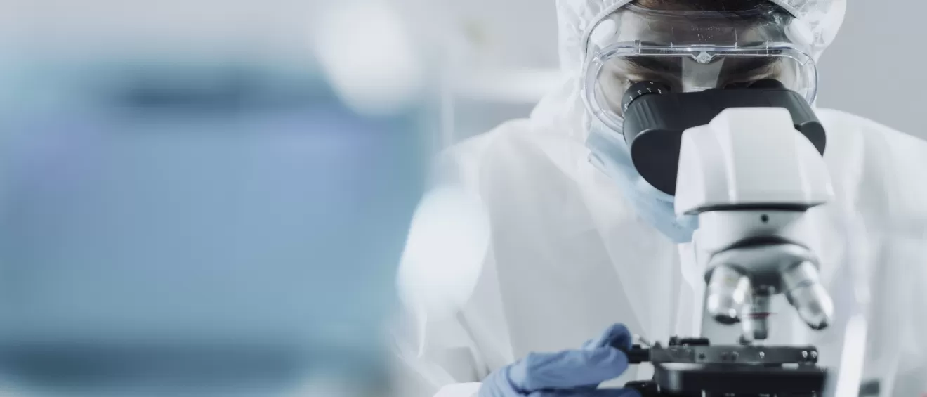 close up of lab technician in full protective clothing using microscope